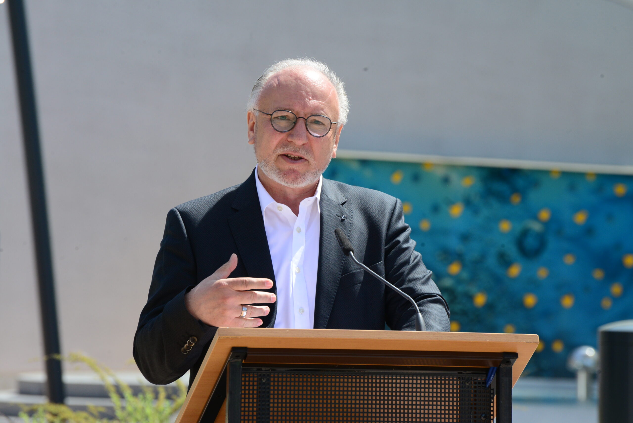 DSC_6524 Ralph Hauboldt steht im Vordergrund, an einem Podium und hält eine Rede.