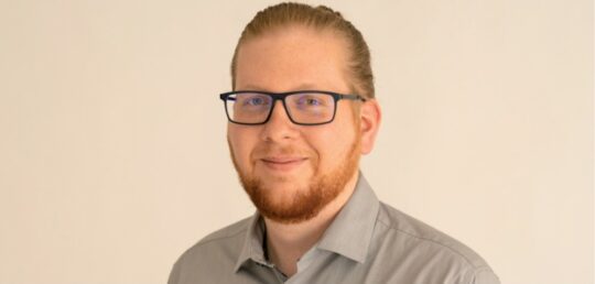 Bild2 Tom Tetzel lächelt, vor einem weißen Hintergrund in die Kamera.
