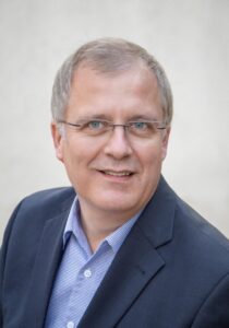 Portraitbild des Vorstandmitgliedes Matthias Marquardt. Er ist Mitte 50, normal gebaut, trägt eine blauen Anzug, hat kurze graue Haare mit sehr deutlichen Geheimratsecken und trägt eine Brille.